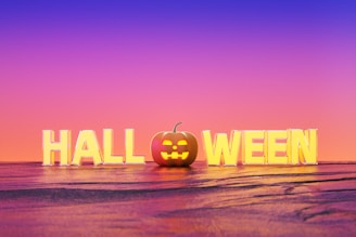 Large block letters spell out 'HALLOWEEN' with a pumpkin in place of the 'O'. The background features a gradient sky transitioning from purple to orange.
