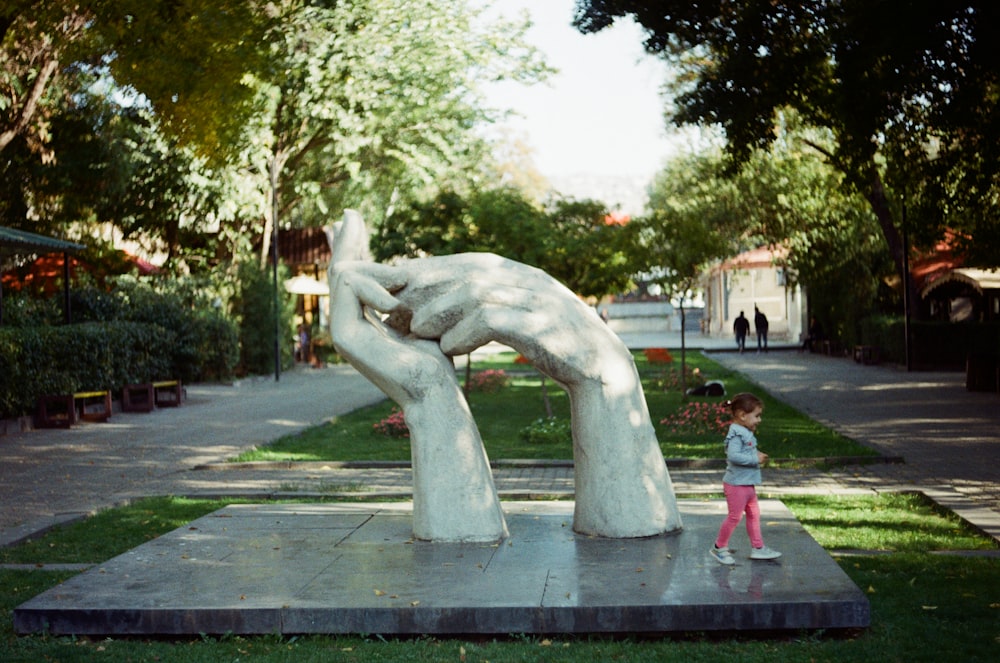 a little girl standing next to a statue of a hand