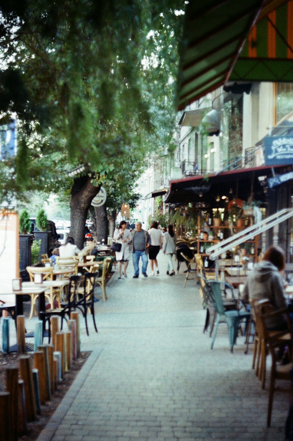 a group of people walking down a sidewalk next to tables and chairs