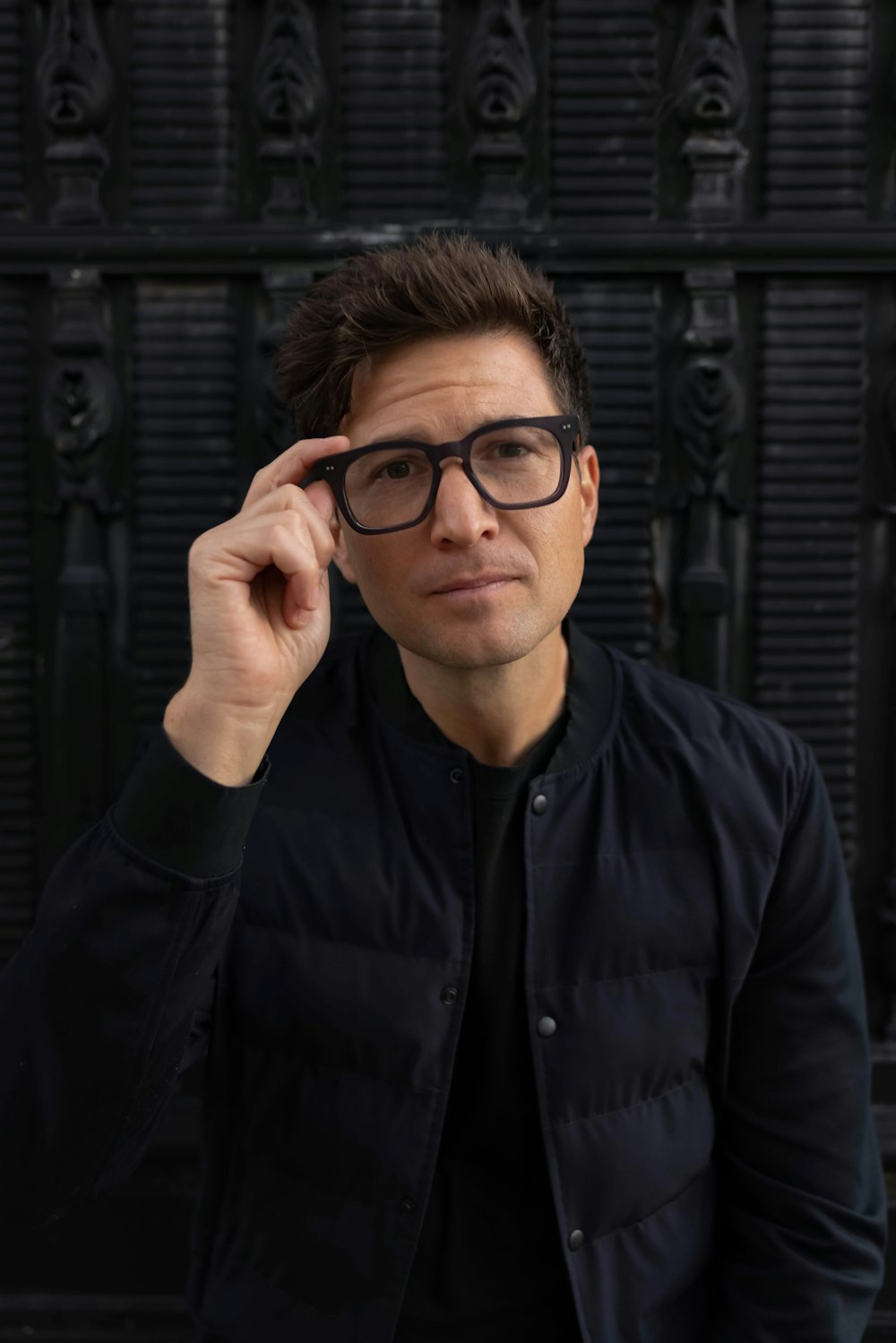 a man wearing glasses sitting in front of a black wall