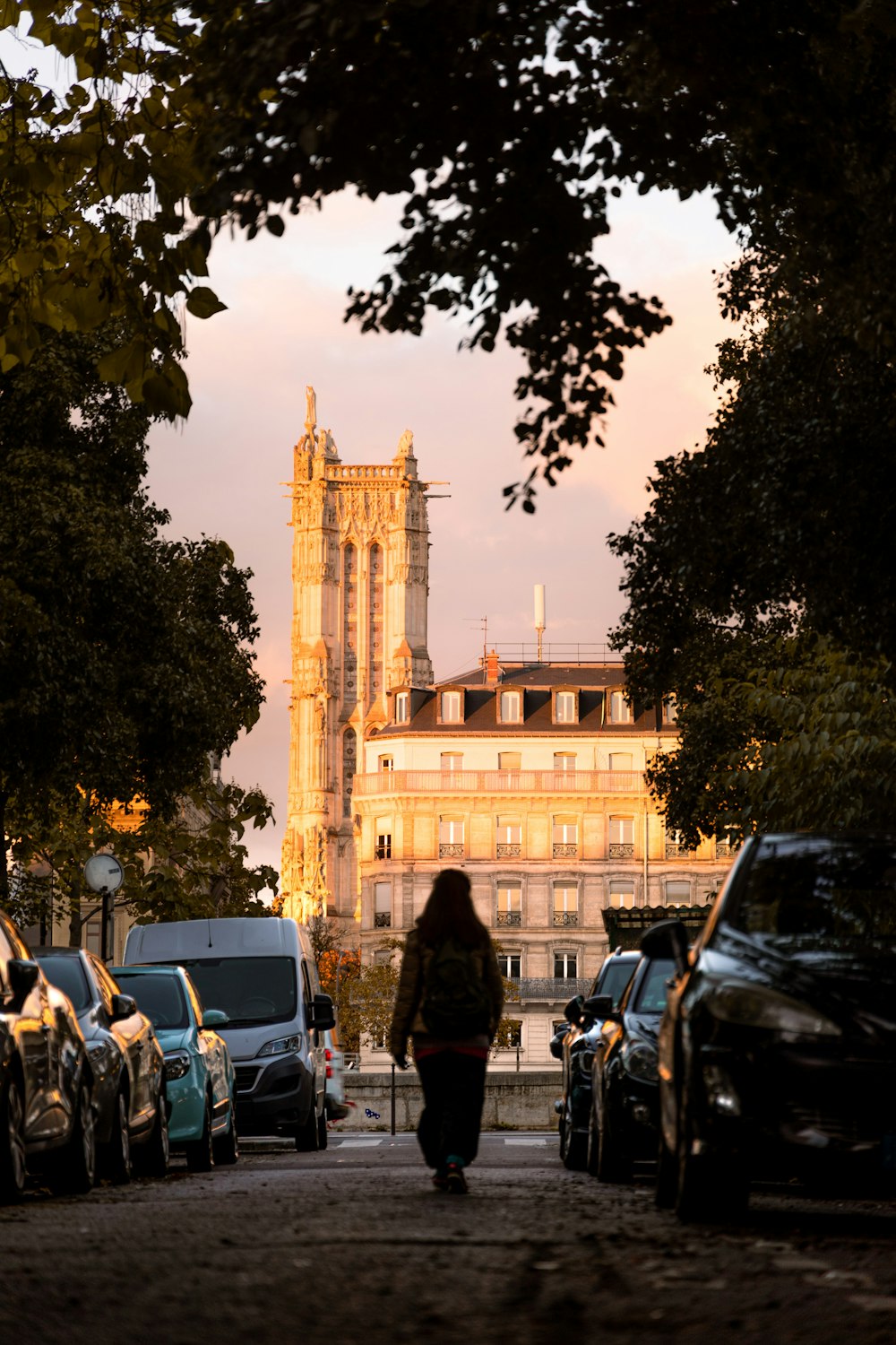 a woman walking down a street next to parked cars