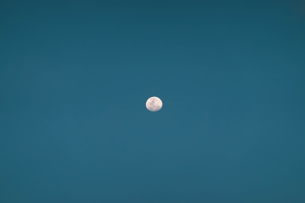a full moon is seen in the blue sky