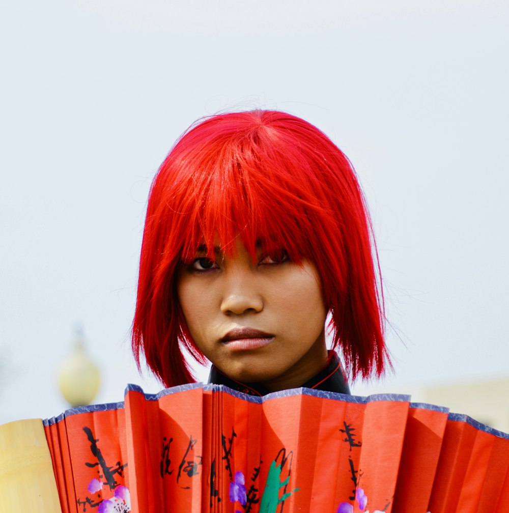 a woman with red hair holding a red fan