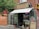 A quaint storefront with a brick exterior and an awning that reads 'Conserve Montreal'. The entrance is glass with a sign indicating 'Groceries'. A small stool and what appears to be a statue of a dog are placed outside. There is a neon 'Ouvert' sign visible in the window, and various product advertisements and boards are displayed on the exterior walls.