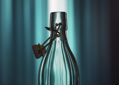 A clear glass bottle with a metal clasp closure is centered against a blurred background of vertical blue and green hues.