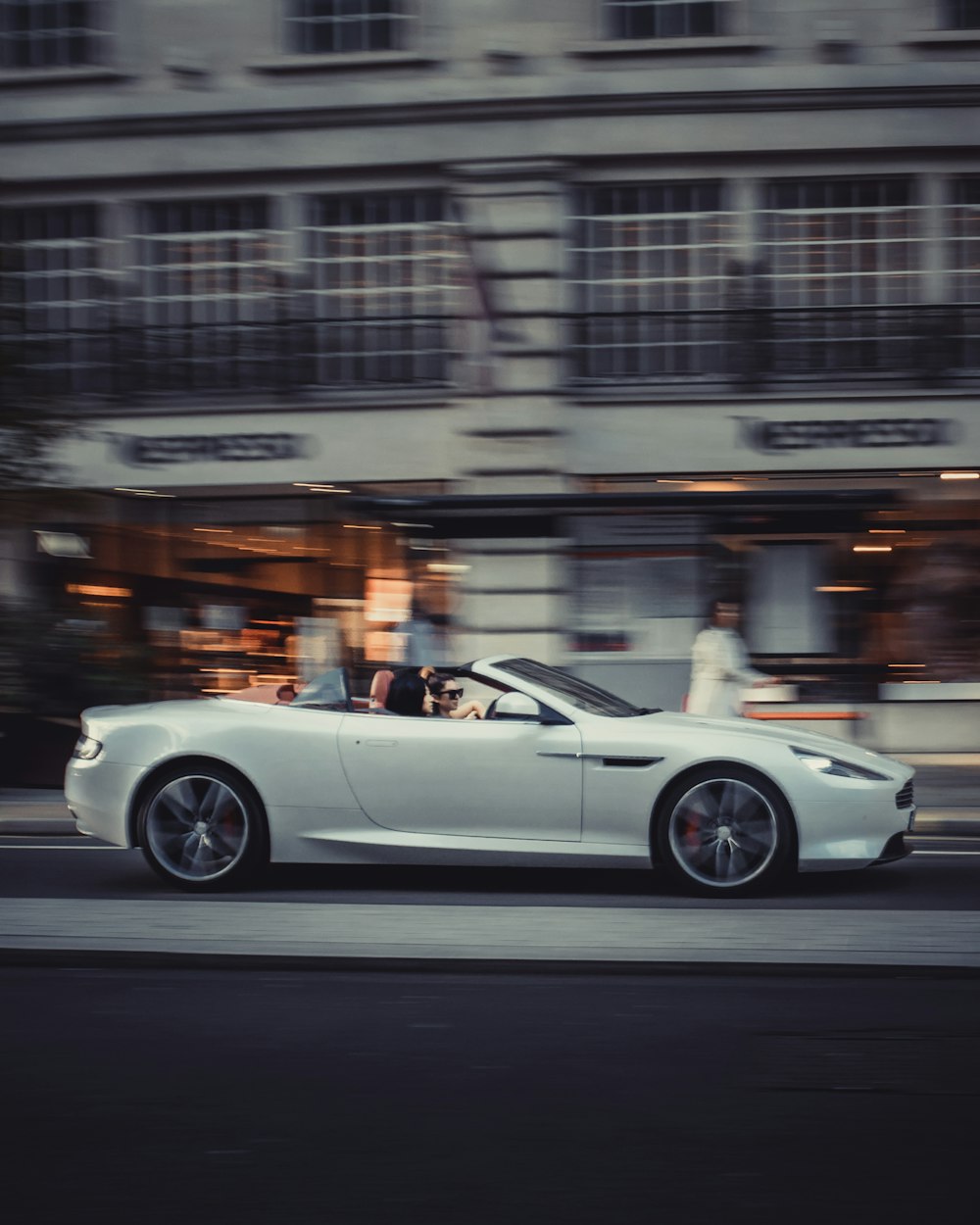 a white sports car driving down a city street