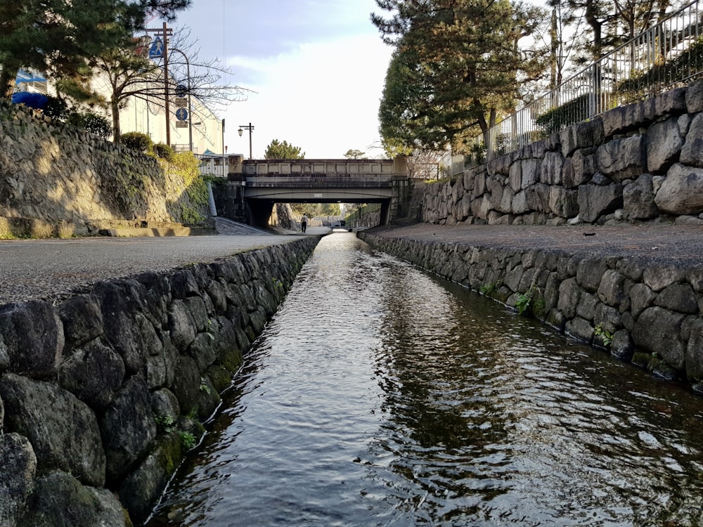 Ein Fluss, der unter einer Brücke neben einer Steinmauer fließt