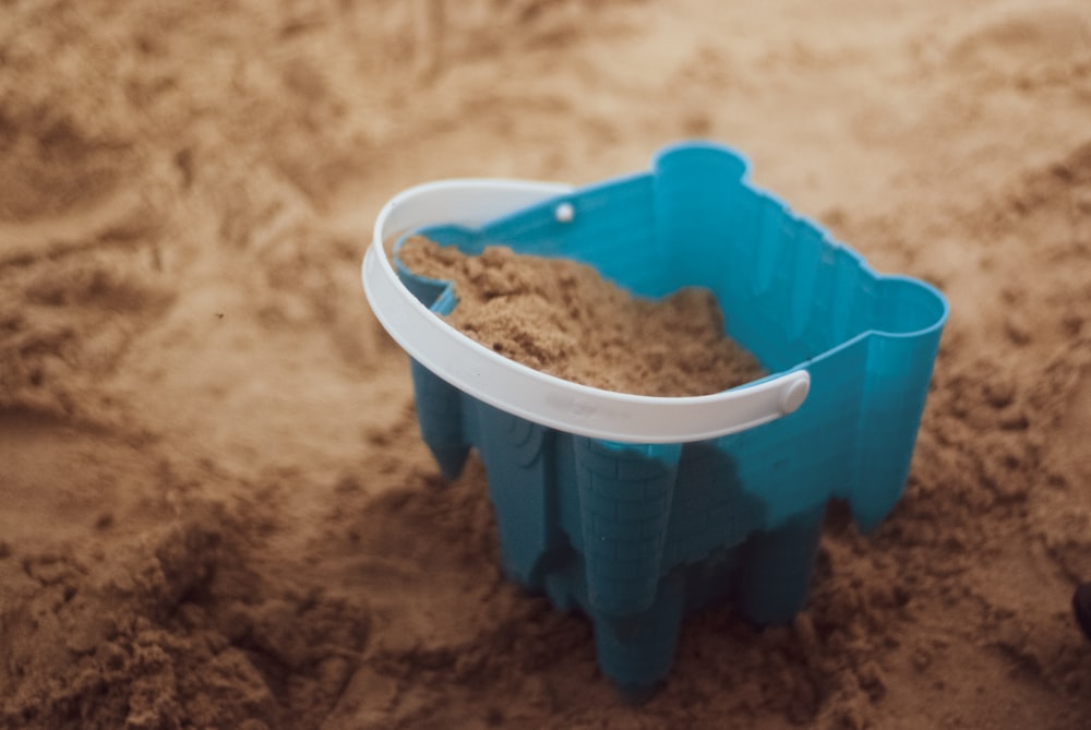 un seau en plastique bleu rempli de sable sur une plage