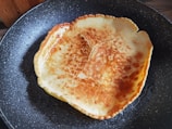 A frying pan mid-flip with golden pancakes in a cozy kitchen setting.