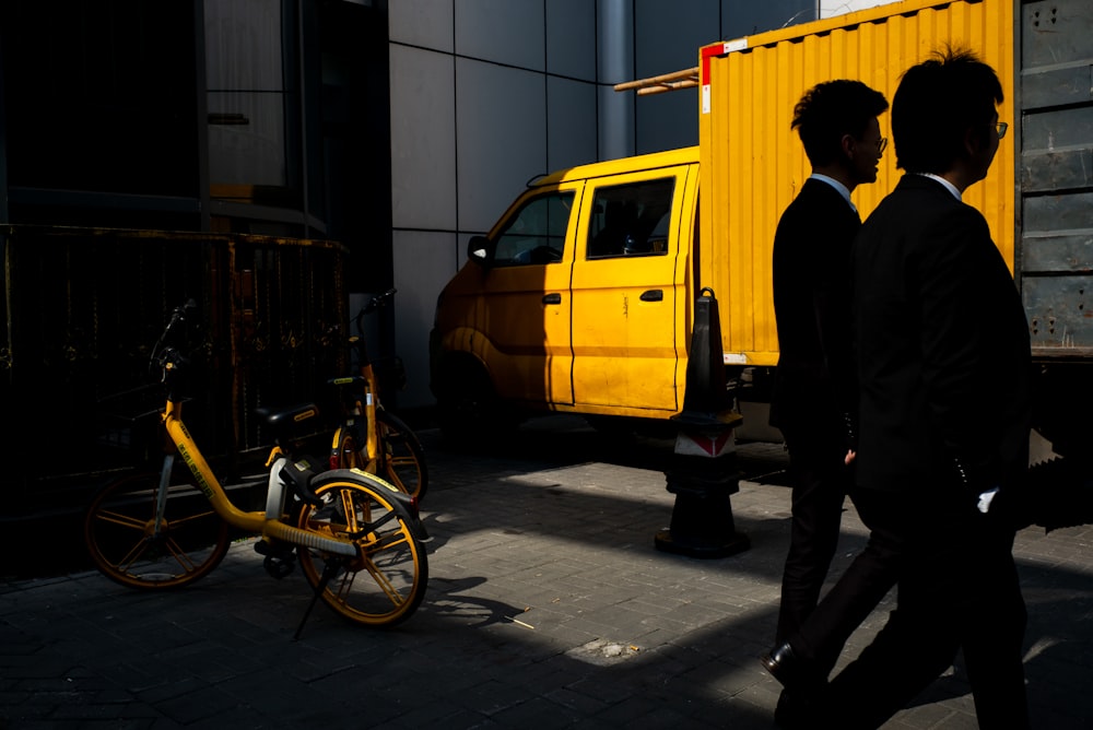 a couple of men walking down a street next to a yellow truck