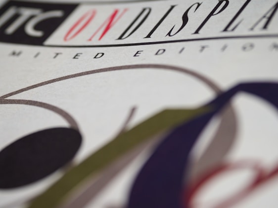 A close-up view of a graphic design featuring the text 'ON DISPLAY' highlighted in red on a white background. The letters are bold and part of a limited edition print design. Curved lines and shapes in black, green, and red are artistically arranged around the text.