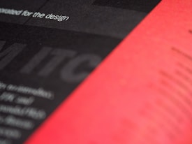 A close-up view of a printed page with a blurred mix of black and red sections. The text 'for the design' is partially visible and the overall appearance is abstract and artistic.