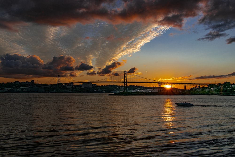 the sun is setting over the water with a bridge in the background