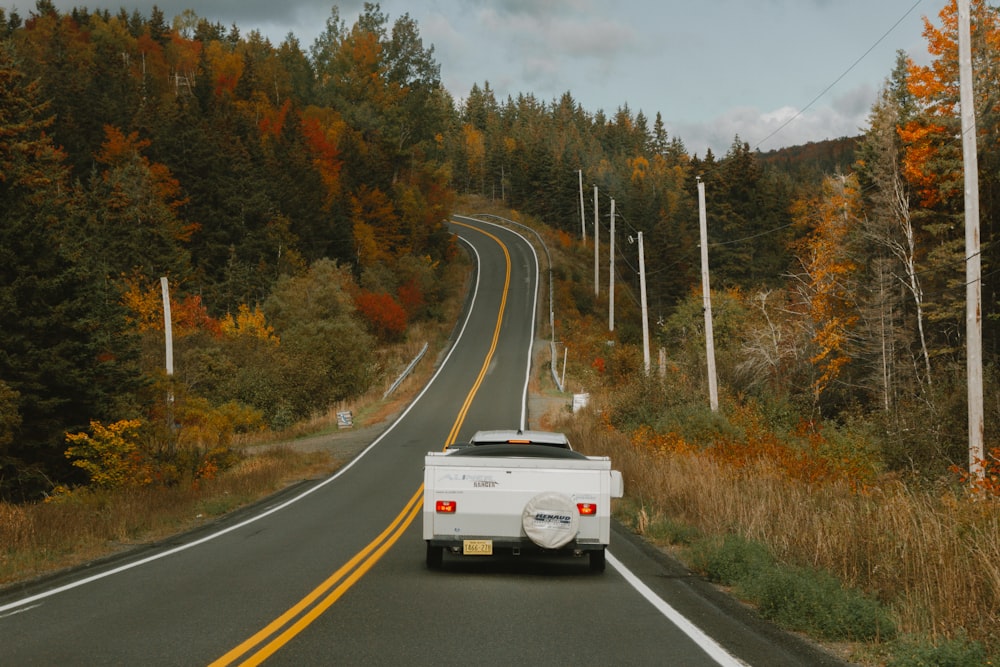 a white truck driving down a road next to a forest