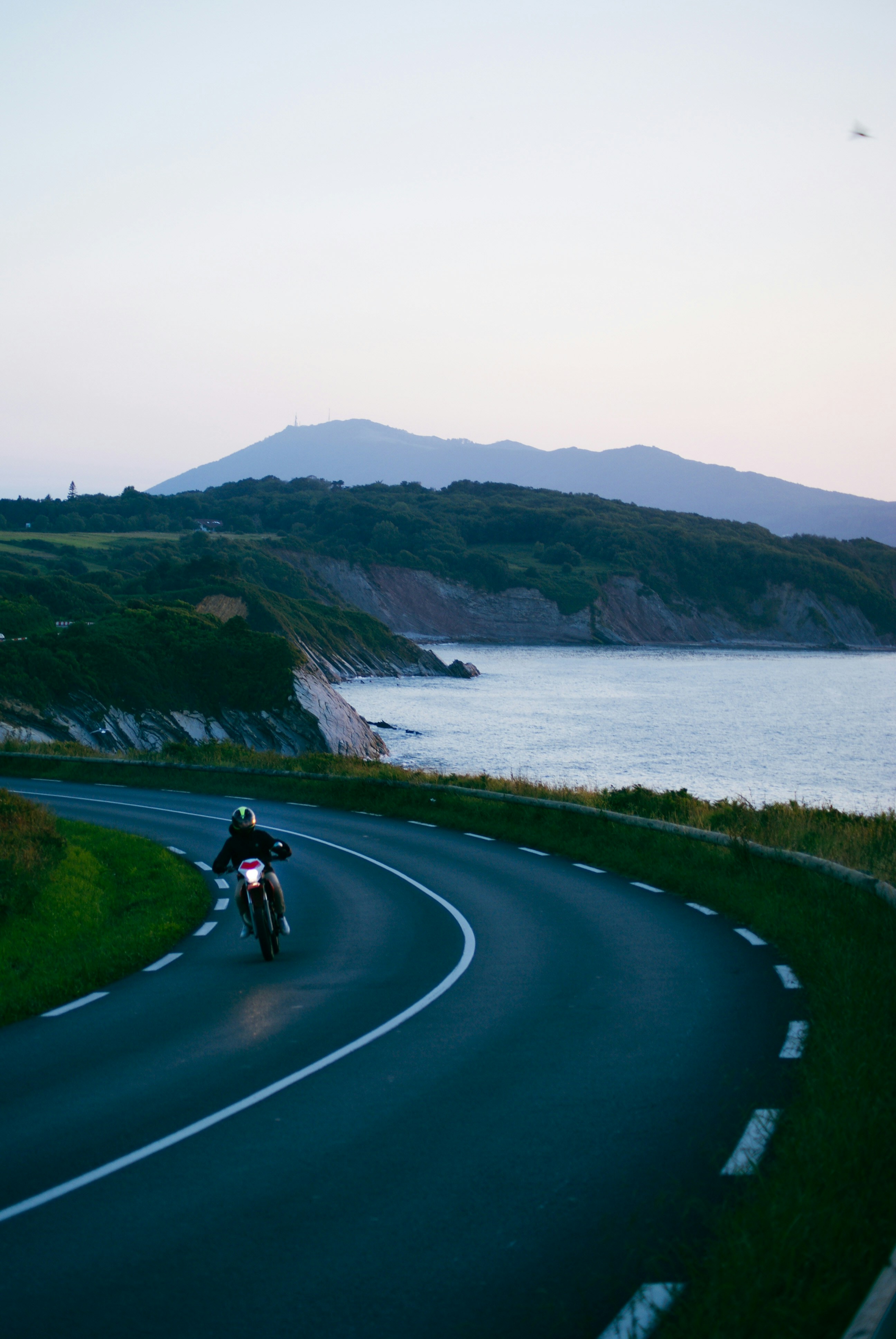 Heavy cruiser motorcycle on coastal Nova Scotia road at dusk, dark atmospheric low-key lighting, shadowed asphalt