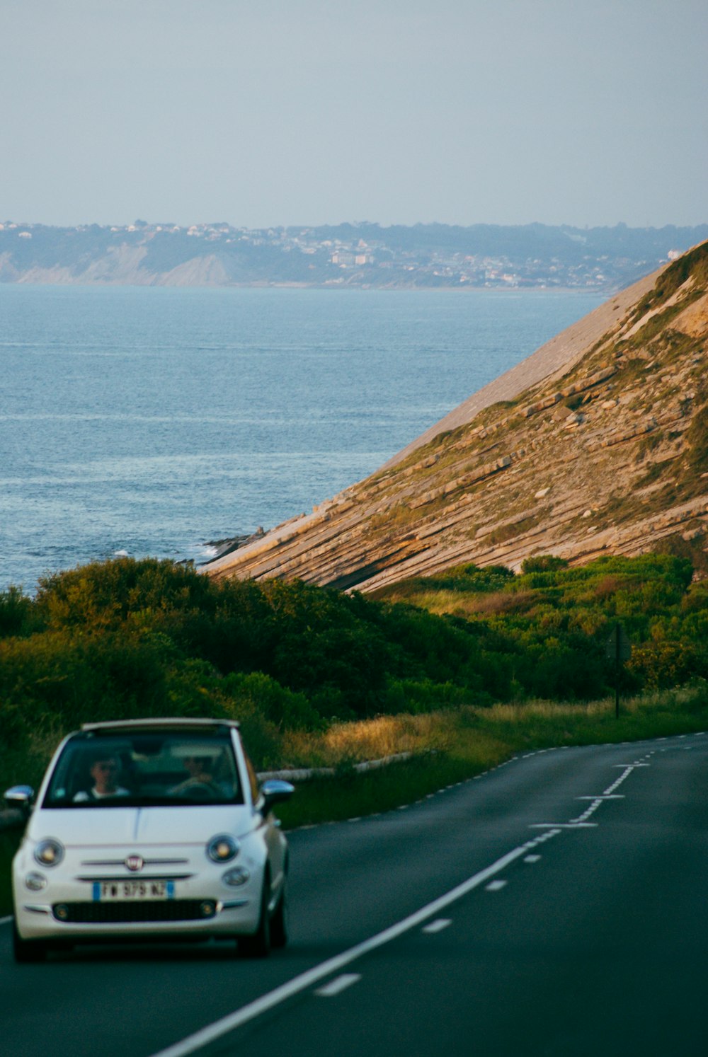 a white car driving down a road next to the ocean