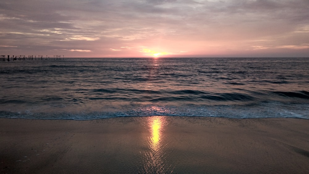 the sun is setting over the water at the beach