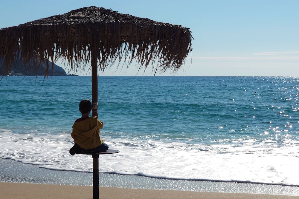 a man sitting under a straw umbrella on the beach