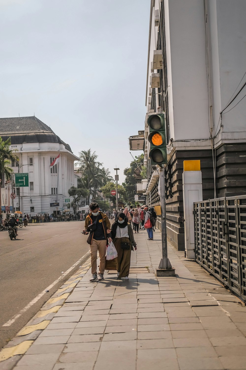 a group of people walking down a sidewalk next to a traffic light