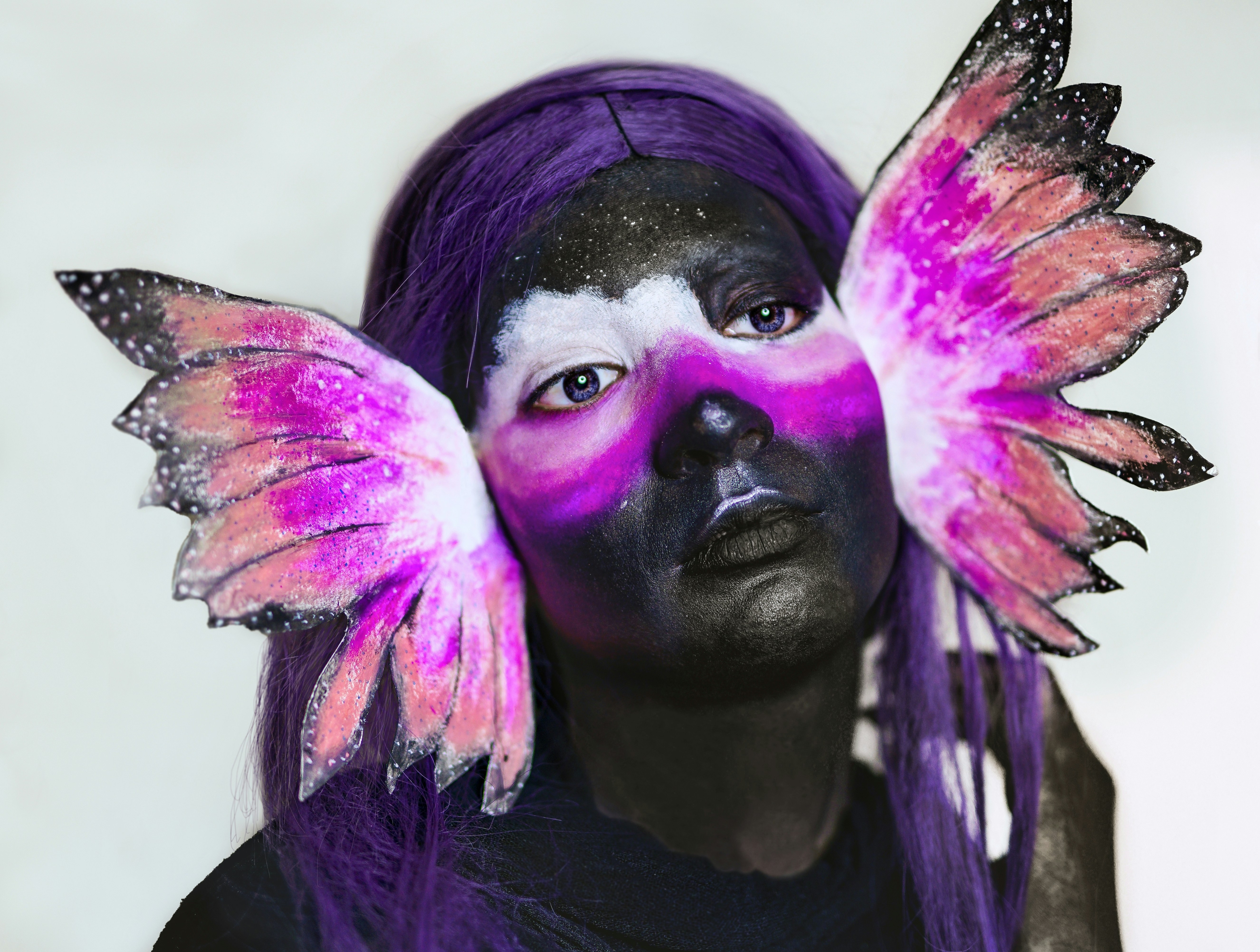 uma mulher com cabelos roxos e asas pintadas em seu rosto