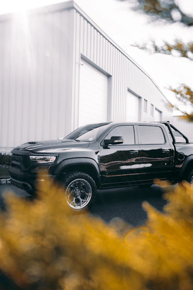A sleek green and gray cargo truck parked at a modern warehouse loading dock during sunset.