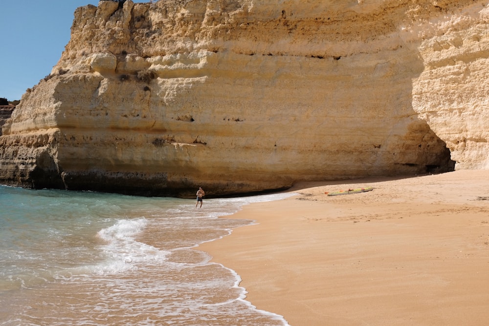 a person standing on a beach next to a cliff