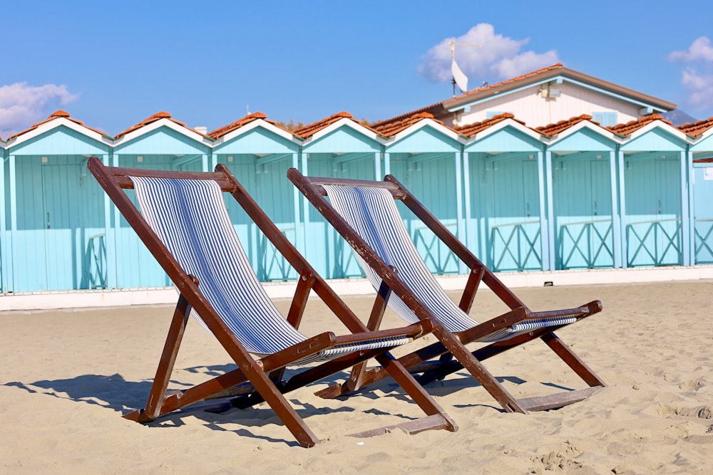 two beach chairs sitting in the sand in front of a building