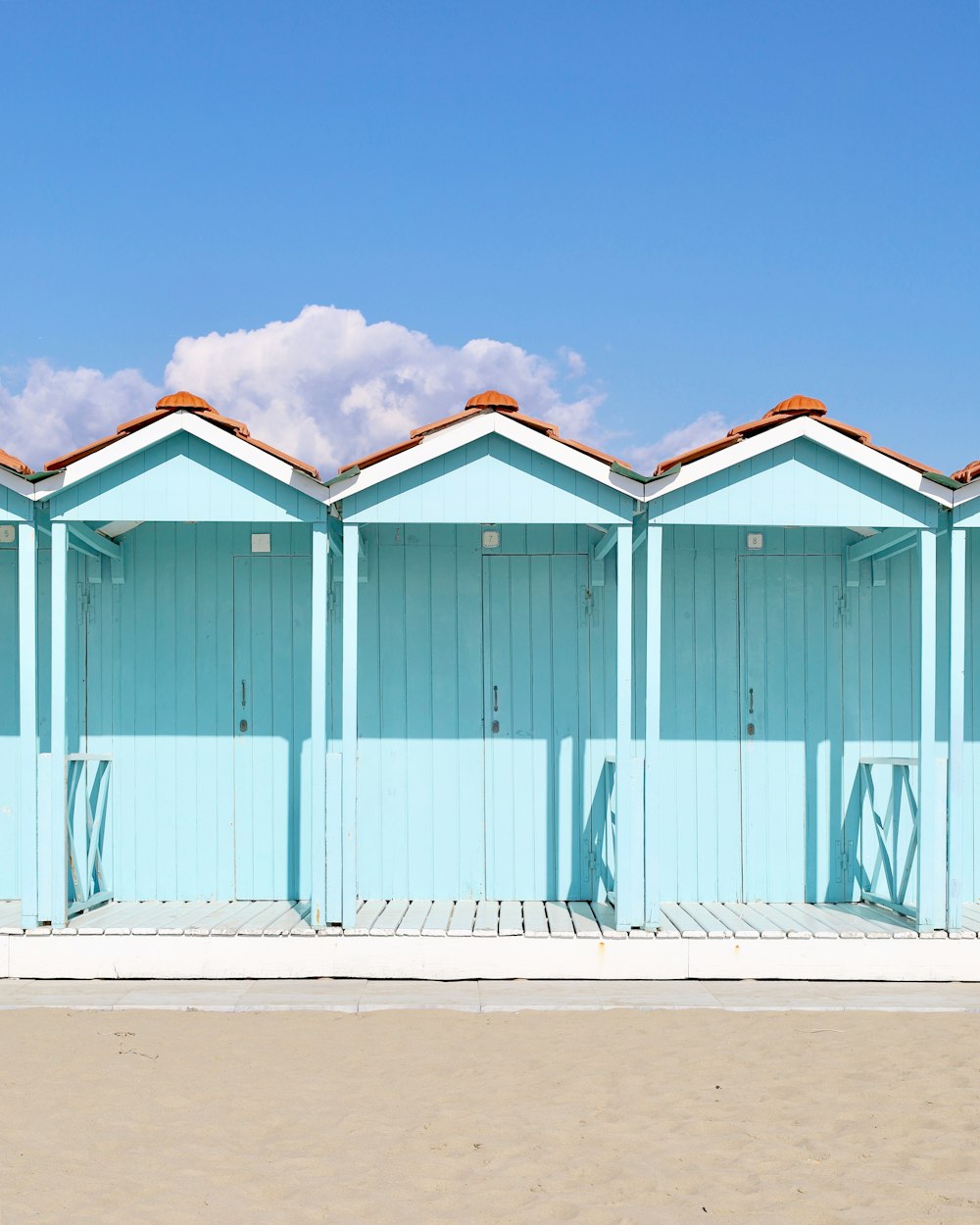 a row of blue beach huts sitting on top of a sandy beach