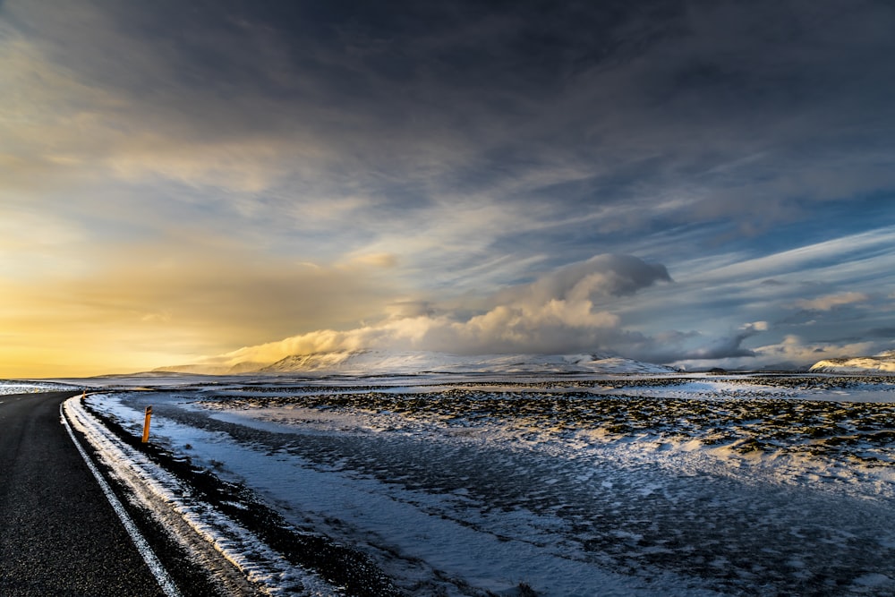 a road with snow on the ground and clouds in the sky