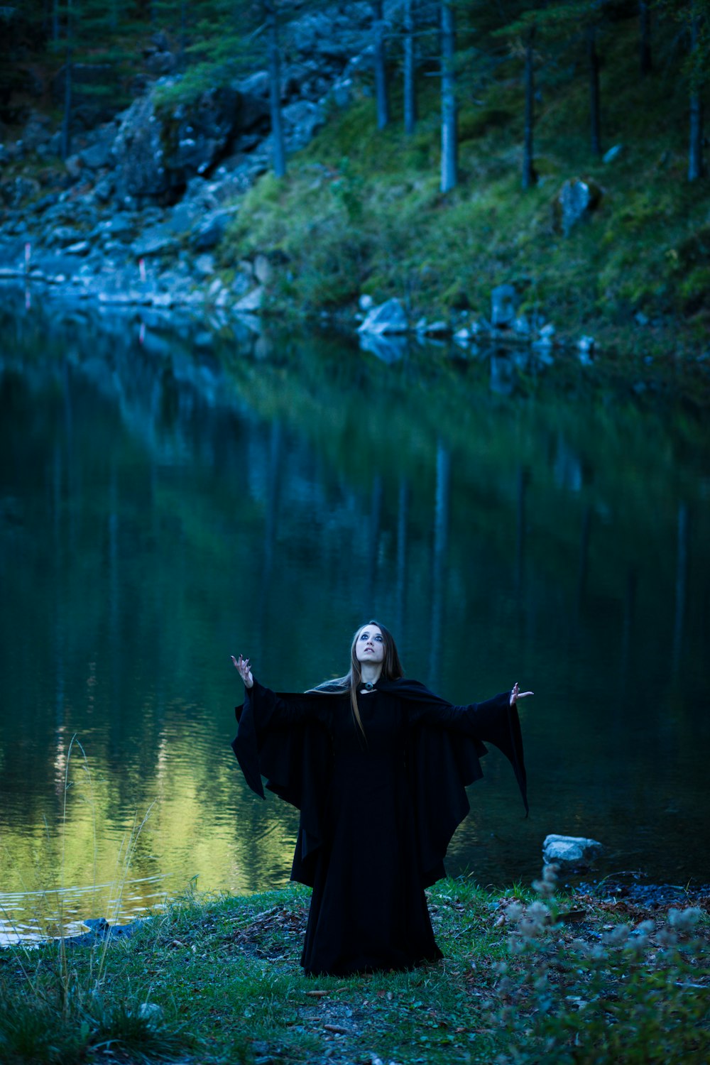 a woman dressed in black standing in front of a lake