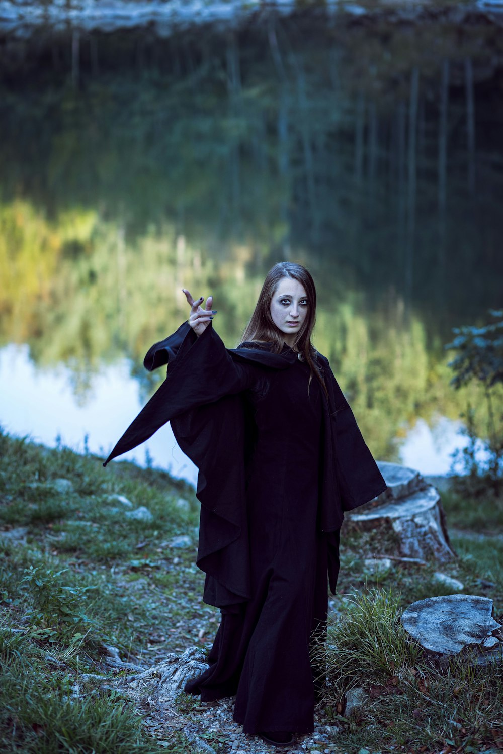 a woman dressed in a black costume standing in front of a lake
