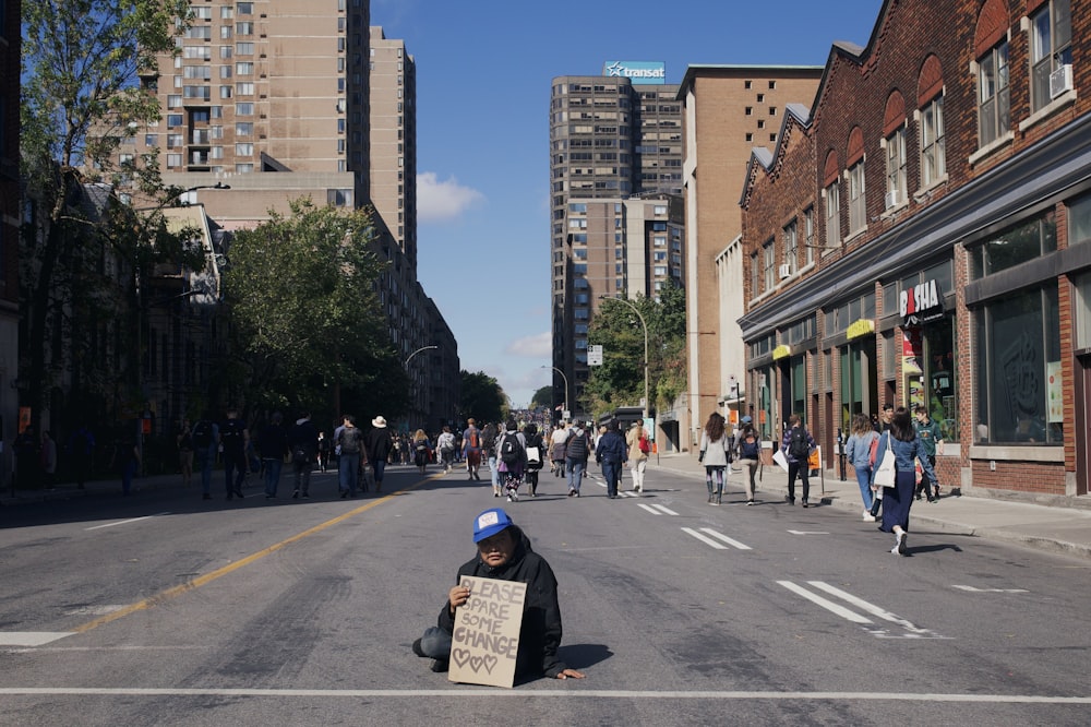 a person sitting in the middle of a street holding a sign