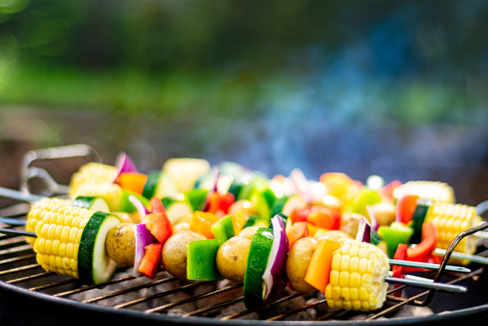 a bbq grill with skewered vegetables and corn on the cob