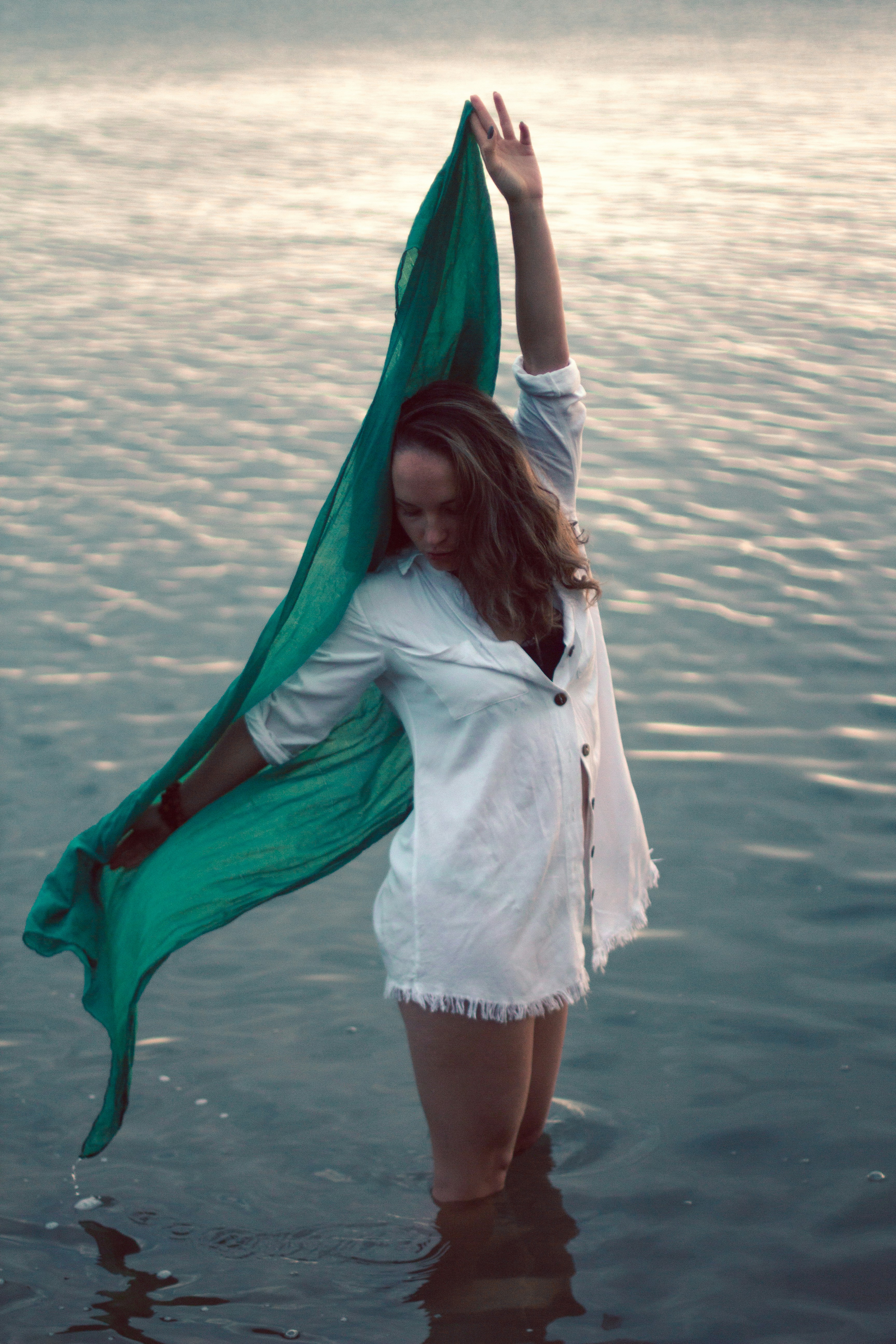 a woman standing in the water holding a green scarf