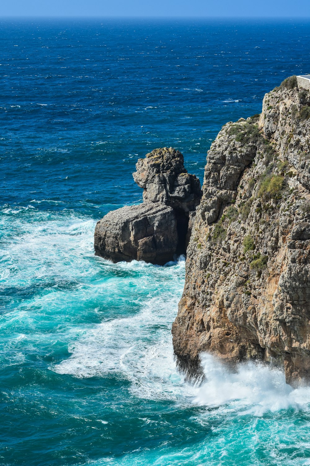 a large rock sticking out of the ocean next to a cliff