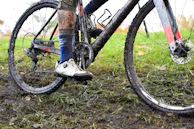Close-up of a cyclist's muddy tires spinning on a rocky gravel path during a challenging ride.
