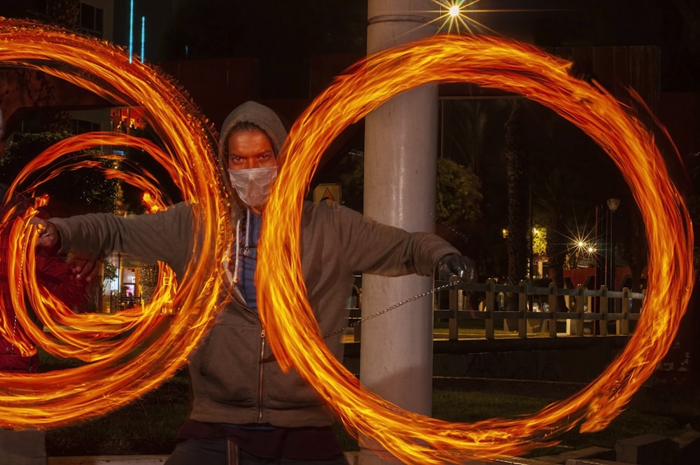 a man in a hoodie and a face mask is holding two fire hoops