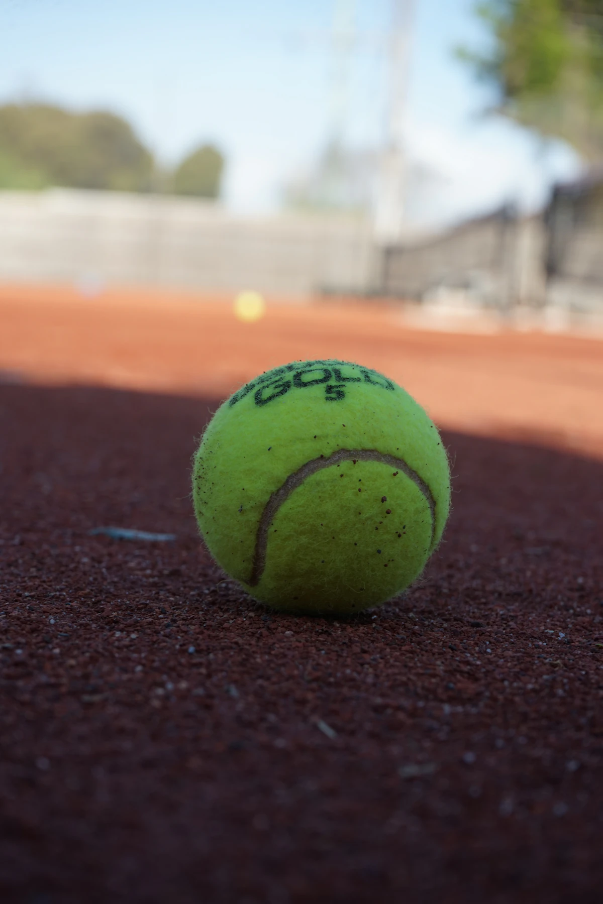 Tennisball auf einem leeren Sandplatz als Symbol für Ballgefühl und Rückschlagspiele