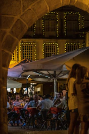A vibrant scene of members enjoying a beautifully set outdoor dinner under string lights, with chefs presenting dishes.