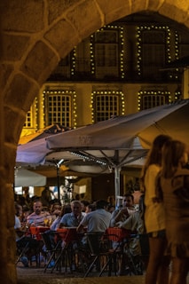 A lively outdoor seating area at sunset, with young people enjoying pizzas and drinks under string lights.