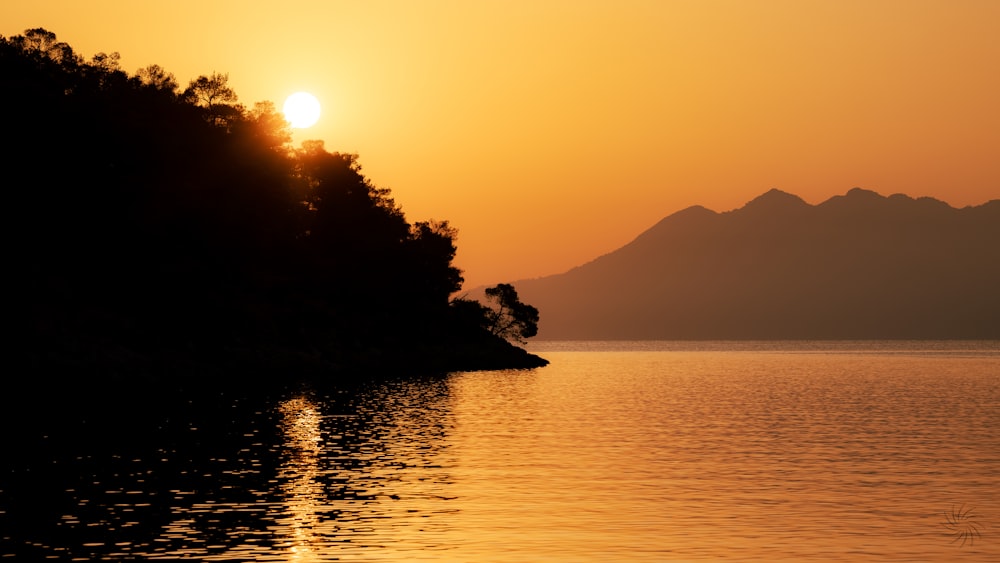 the sun is setting over a lake with mountains in the background