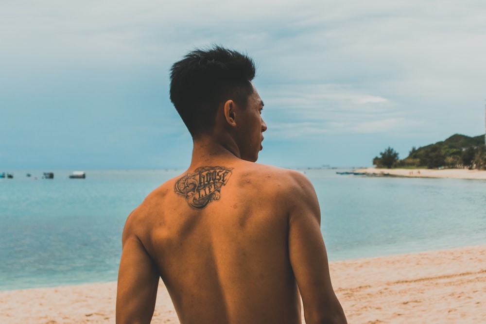 a man with a tattoo on his back standing on a beach