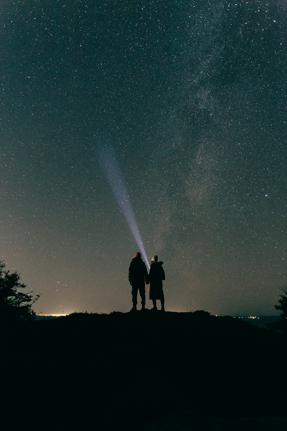 two people standing on top of a hill under a night sky
