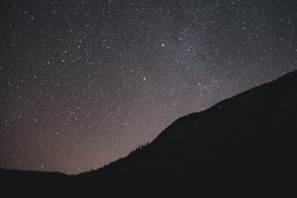 the night sky with stars above a mountain