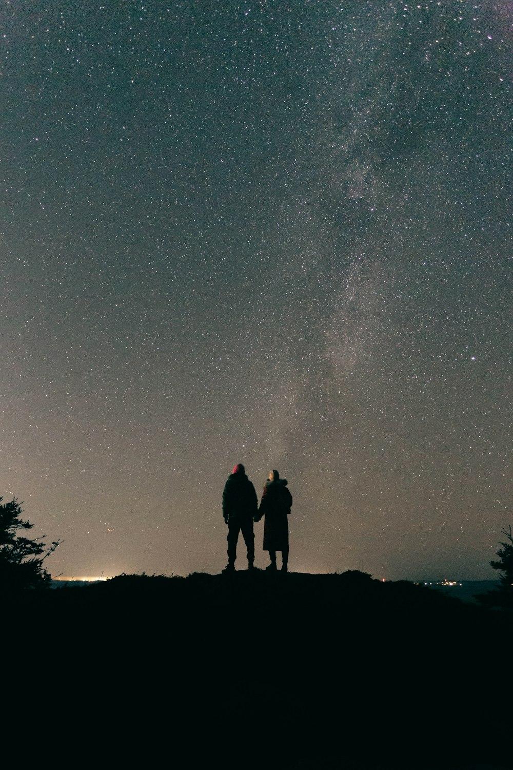 two people standing on top of a hill under a night sky