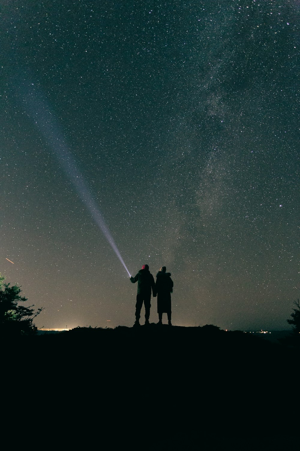 two people standing on top of a hill under a night sky