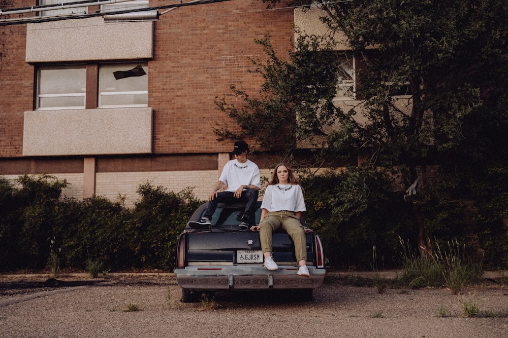 a man and a woman sitting on top of a car