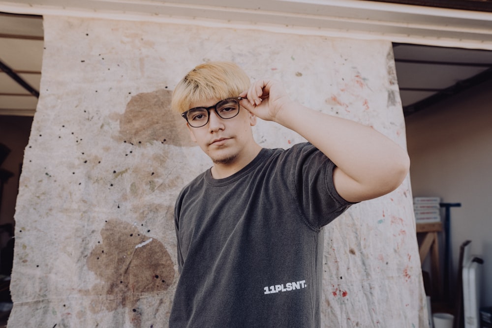 a man wearing glasses standing in front of a wall