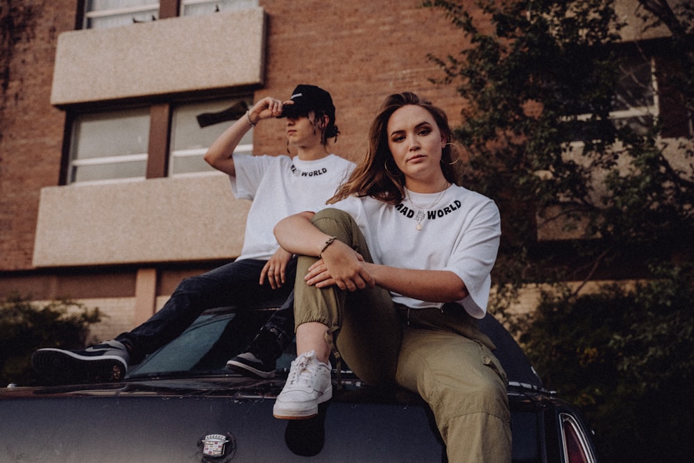 two people sitting on the hood of a car