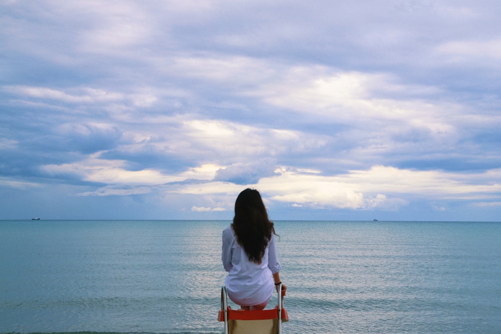a woman sitting on a chair looking out at the ocean